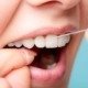 Gros plan sur une personne utilisant du fil dentaire pour nettoyer entre ses dents blanches, illustrant l'importance de l'hygiène bucco-dentaire.