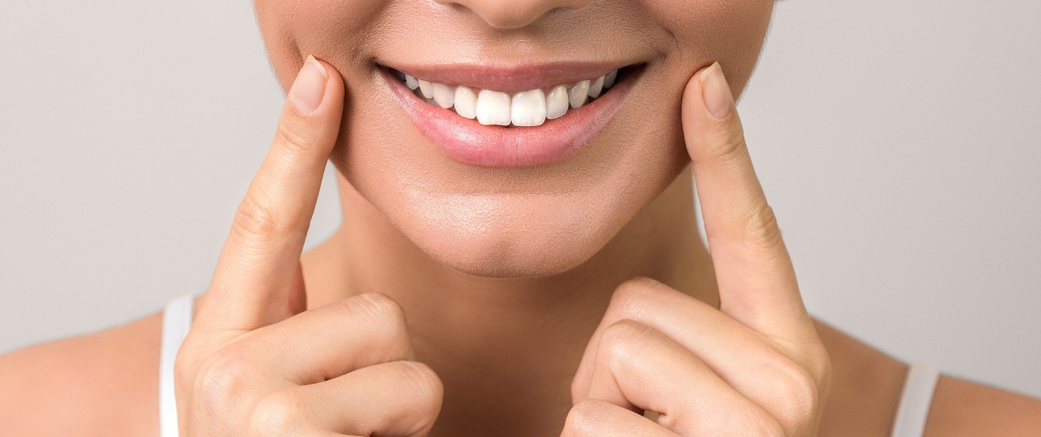 Gros plan sur la bouche d'une femme souriante montrant ses dents blanches, avec ses doigts pointant vers ses joues.