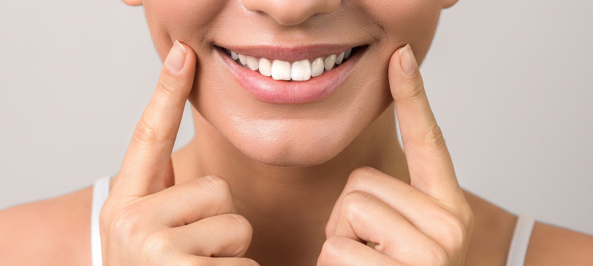 Gros plan sur la bouche d'une femme souriante montrant ses dents blanches, avec ses doigts pointant vers ses joues.